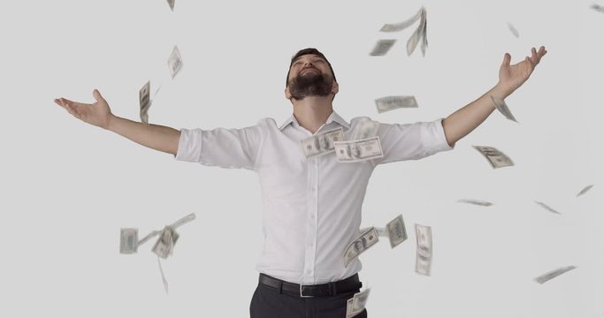 Businessman standing with arms outstretched under raining banknotes over white background