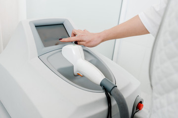 Closeup of cosmetologist using laser machine in beauty salon
