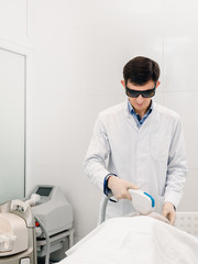 Male doctor cosmetologist in protective glasses doing laser treatment