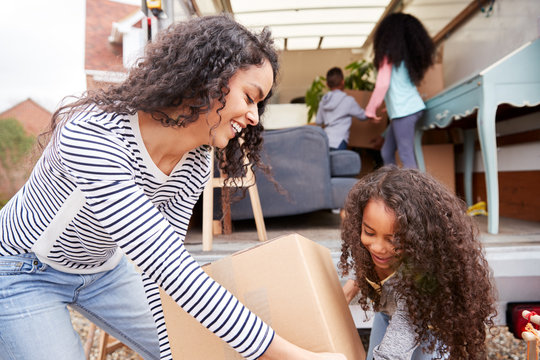 Mother And Children Unloading Furniture From Removal Truck Into New Home