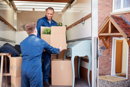 Removal Company Workers Unloading Furniture And Boxes From Truck Into New Home On Moving Day