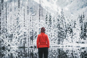 One girl hiker stands in front of a winter lake looking to the snowy landscape. Rear view. - Powered by Adobe