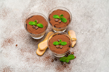 Classic tiramisu dessert in a glass cup and savoiardi cookies on concrete background