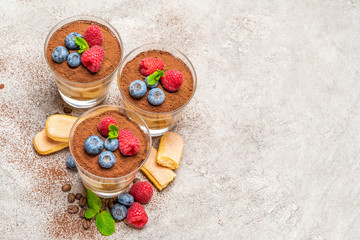 Classic tiramisu dessert with blueberries and raspberries and savoiardi cookies in a glass on concrete background
