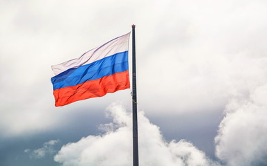 The developing Russian flag tricolor on background of gray cloudy sky