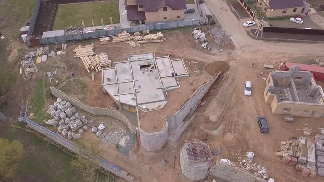 Aerial view of new modern cottage near the building site, construction materials and workers pouring concrete for the foundation. Clip. Process of new building construction.