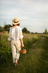 A young redhead woman holding a basket of ripe peaches and walking on the countryside road