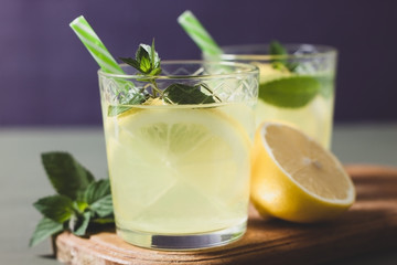 Two glass with lemonade or mojito cocktail with lemon and mint, cold refreshing drink or beverage with ice on rustic blue background. Copy space