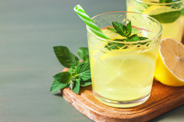 Two glass with lemonade or mojito cocktail with lemon and mint, cold refreshing drink or beverage with ice on rustic blue background. Copy space