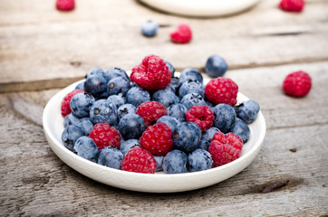 Still life with a blueberries and raspberries on an old wooden table, at the garden. Rural natural food style.