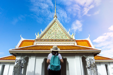 Woman traveler with green backpack and hat at Wat Arun Temple in Bangkok Thailand.