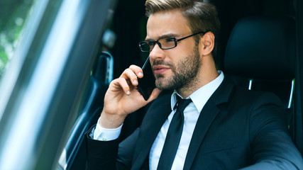 Handsome young businessman in full suit talking on the smart phone while driving car