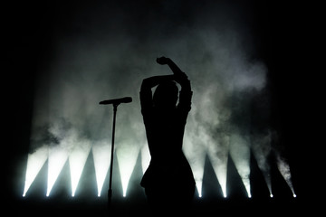 Silhouette of singer on stage. Dark background, smoke, spotlights