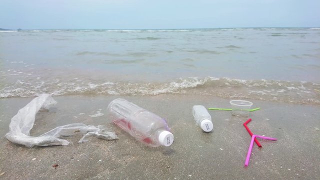 Colorful plastic straws cup bottle bag single use on the sand in the ocean with ocean waves. The people throwing trash carelessly in anywhere not a bin. Environment negligently concept.