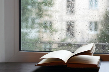 Open book on a wet window, the rain drops on the glass