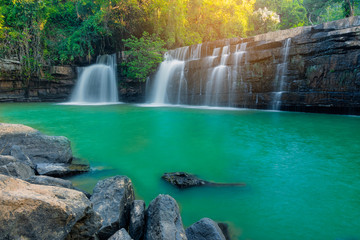 Sri Dit Waterfall is a single-level waterfall with streams flowing through the cliff and rock layer, with sunlight in jungle.
