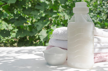 Laundry detergent, fresh washed towels on the white surface in the shadow of leaves