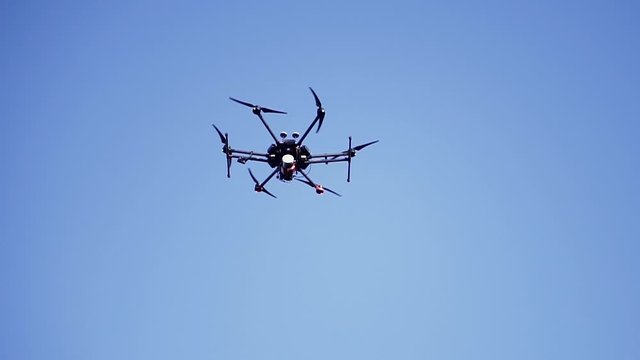 Black drone flying against the blue sky with spinning blades, bottom view. Clip. Compact quadcopter controlled by wireless remote shooting video footages and photos.