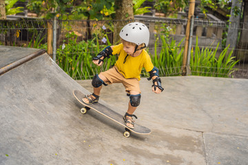 Athletic boy in helmet and knee pads learns to skateboard with in a skate park. Children education, sports