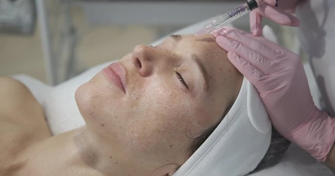 Beautiful woman getting cosmetic injection of botox in forehead
