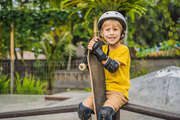 Athletic boy in helmet and knee pads learns to skateboard with in a skate park. Children education,...