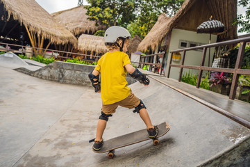 Athletic boy in helmet and knee pads learns to skateboard with in a skate park. Children education, sports