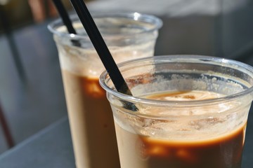 Close up view of ice coffees in glasses with straws. Cold brewed coffee with milk in plastic glasses on dark background. Selective focus.