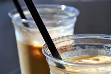 Close up view of ice coffees in glasses with straws. Cold brewed coffee with milk in plastic glasses on dark background. Selective focus.