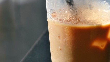 Close up view of ice coffee in glass with straw. Cold brewed coffee with milk in glass on dark...