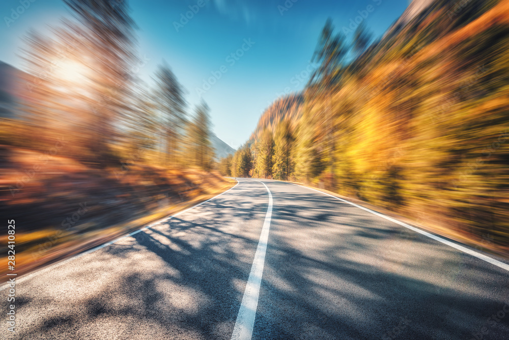 Wall mural mountain road in autumn forest at sunset with motion blur effect. asphalt road and blurred backgroun