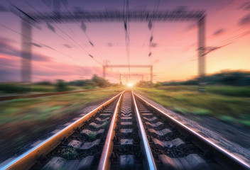 Railroad and beautiful sky at sunset with motion blur effect in summer. Industrial landscape with railway station and blurred background with colorful sky.  Railway platform in speed motion. Sleepers