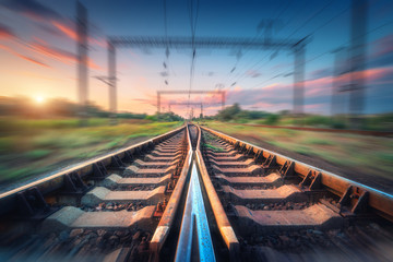 Railroad and beautiful sky at sunset with motion blur effect in summer. Industrial landscape with railway station and blurred background with colorful sky.  Railway platform in speed motion. Sleepers