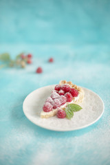 Tarta z malinami na białym talerzyku na niebieskim tle  świeże maliny , ciastko z malinami , tarta z malinami  i cukrem pudrem © Aga