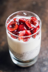 Plain yogurt with chia seed, muesli and cherries in glass on the rustic wooden background. Selective focus. 