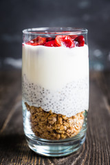 Plain yogurt with chia seed, muesli and cherries in glass on the rustic wooden background. Selective focus. 