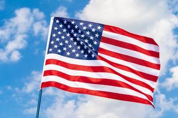 American flag on flagpole waving in the wind against white clouds