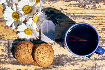 Fresh brewed chamomile tea. on the table are flowers and cookies.