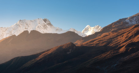 Beautiful mountains with snowy peaks at sunny morning in Nepal. Silhouettes of  Himalayan mountains at sunrise. Colorful landscape with high rocks, blue sky and gold sunbeam. Amazing Himalayas. Nature