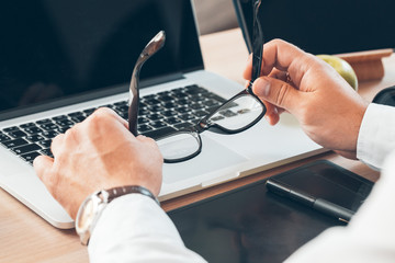 Man sitting at desk at home and hold his glasses.