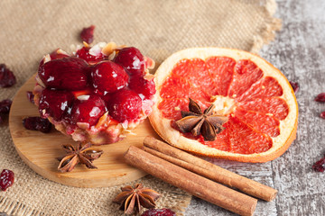 Fresh fruit and berry tart dessert with toss sugar on wooden background. Delicious sweet cake with raspberries, grapes, strawberries, cherry, kiwi, grapefruit and cream.