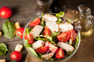 Fresh salad made of tomato, ruccola, chicken breast, eggs, arugula, crackers and spices. Caesar salad in a white, transparent bowl on wooden background