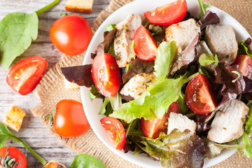 Fresh salad made of tomato, ruccola, chicken breast, eggs, arugula, crackers and spices. Caesar salad in a white, transparent bowl on wooden background