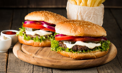 Close-up photo of home made hamburger with beer made of beef, onion, tomato, lettuce, cheese and spices. Fresh burger closeup on wooden rustic table with potato fries and chips.