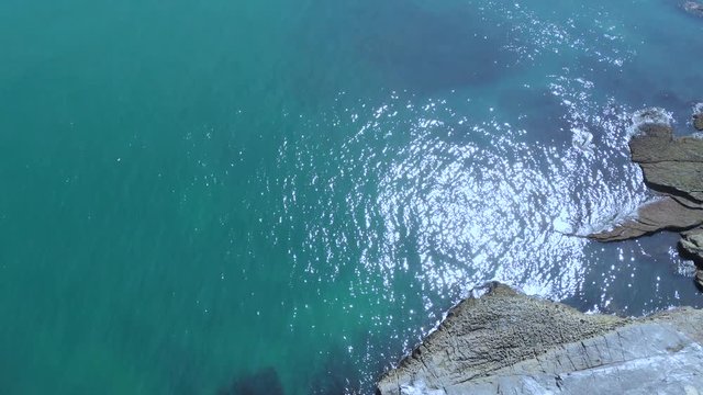 An aerial forward reveal footage of a rocky coastline toward two islands rock with turquoise water under a majestic blue sky