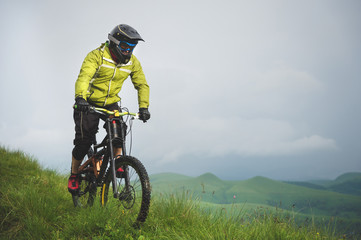 Fototapeta na wymiar Front view of a man on a mountain bike standing on a rocky terrain and looking down against a gray sky. The concept of a mountain bike and mtb downhill