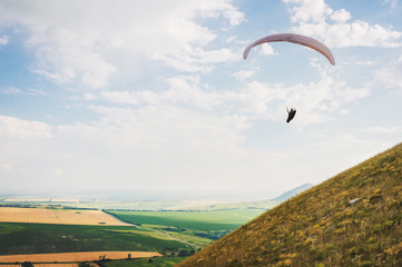 A paraglider flies in the sky in a cocoon suit on a paraglider over the Caucasian countryside with hills and mountains. Paragliding Sport Concept