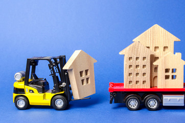 A yellow forklift loads a wooden figure of a house into a truck. Concept of transportation and...