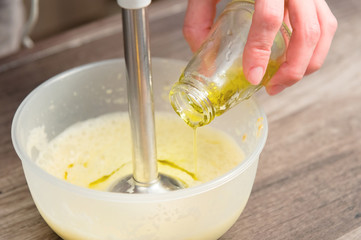 close-up whipping the mixture of homemade mayonnaise with a blender in a plastic bowl. olive oil