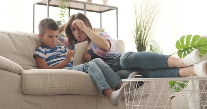 Mother with her son writing in notepad while relaxing on sofa at home