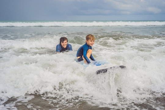 Father or instructor teaching his 5 year old son how to surf in the sea on vacation or holiday. Travel and sports with children concept. Surfing lesson for kids